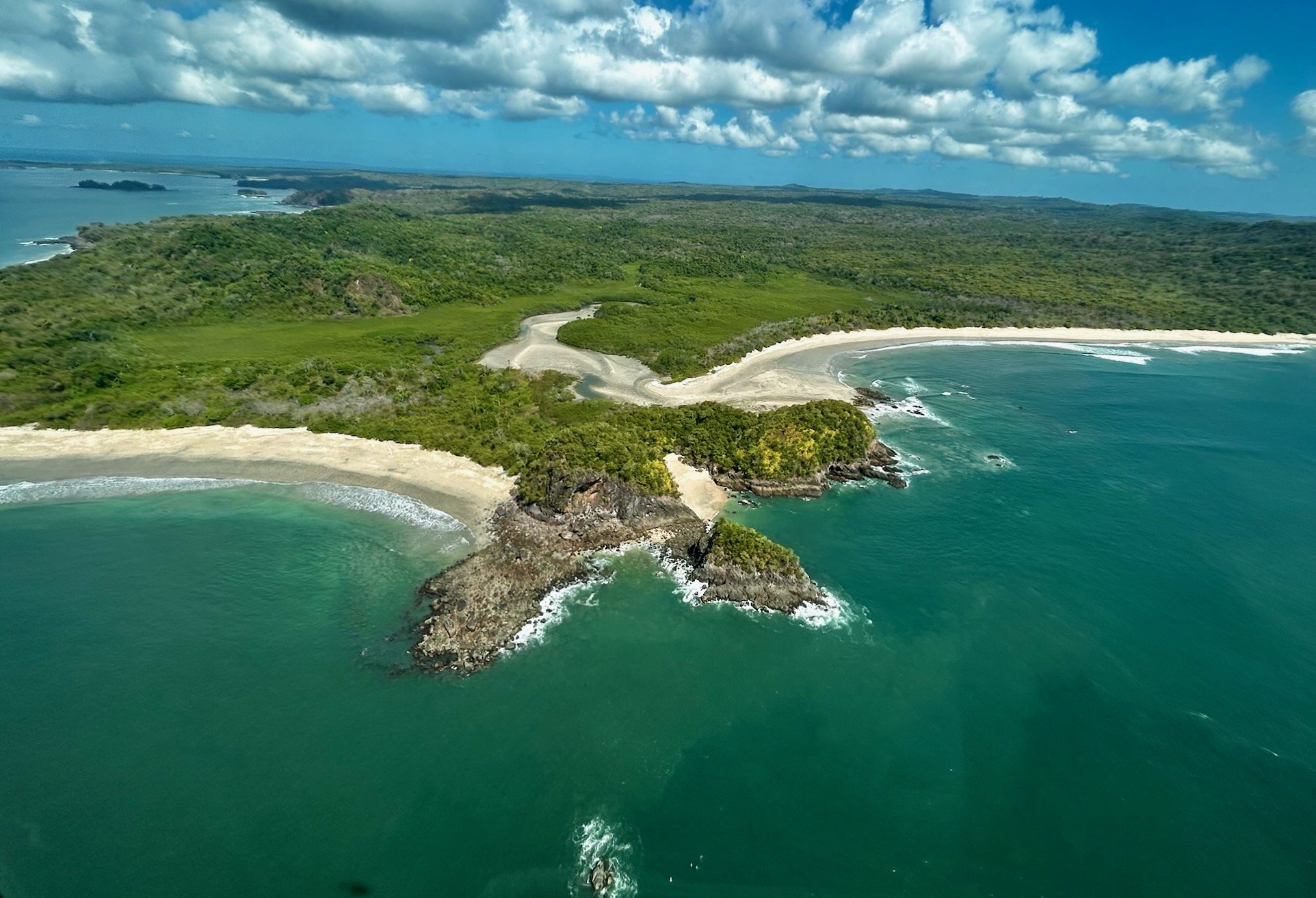 A headland between two beaches, with the river estuary and unbroken forest behind, on the Pacific coast of Isla del Rey